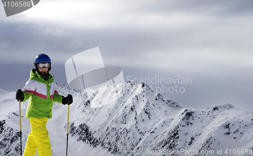 Image of Young skier with ski poles in sunlight mountains and cloudy gray