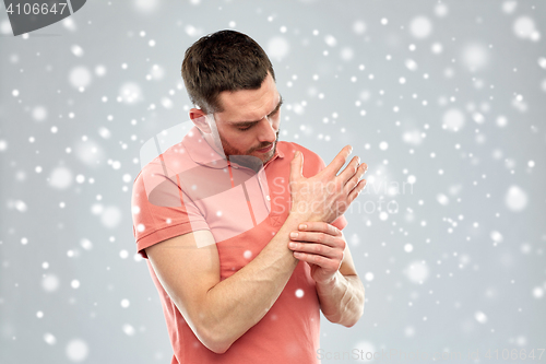 Image of unhappy man suffering from pain in hand over snow