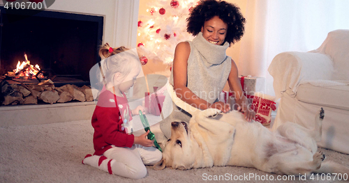 Image of Mom and daughter in sweaters play with pet dog