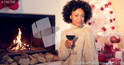 Image of Pretty woman holds wine glass beside fireplace