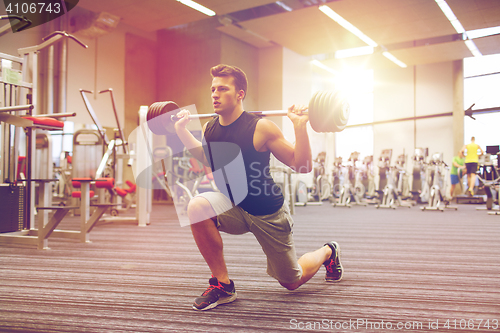 Image of young man flexing muscles with barbell in gym