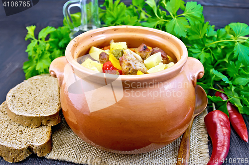 Image of Roast meat and vegetables in clay pot on dark board