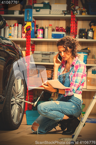 Image of car mechanic woman in blue overalls talking on the phone near a 