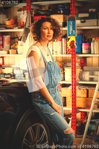 Image of curly-haired woman in blue overalls mechanic near a car 