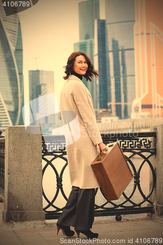 Image of smiling woman in a bright coat with wooden case in her hand