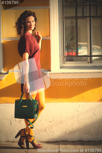 Image of beautiful smiling woman in a burgundy dress with green handbag