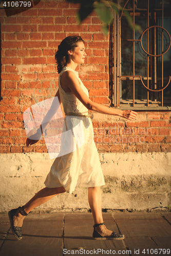 Image of beautiful woman in a white dress goes on old street