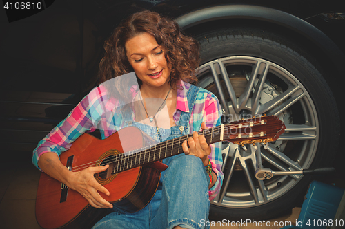 Image of woman car mechanic with guitar in garage