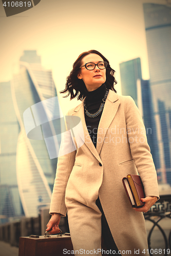 Image of beautiful brunette in light coats with books and wooden briefcas