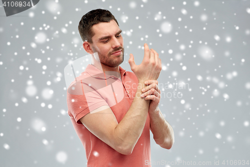 Image of unhappy man suffering from pain in hand over snow