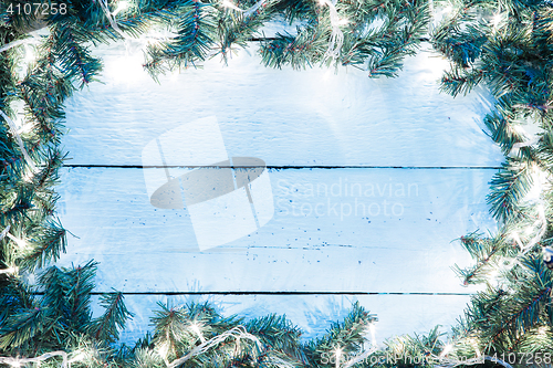 Image of Christmas light blue wooden background with lightbulb and spruce branches