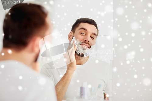 Image of happy man applying shaving foam at bathroom mirror