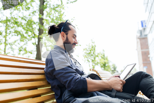 Image of man with tablet pc sitting on city street bench