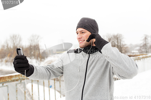 Image of happy man with earphones and smartphone in winter