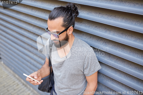 Image of man with bag texting on smartphone in city