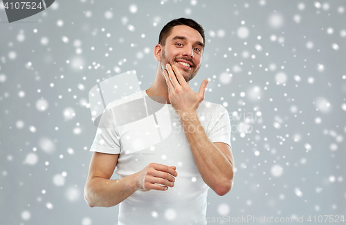 Image of happy young man applying cream or lotion to face