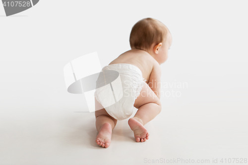 Image of little baby in diaper crawling on white floor