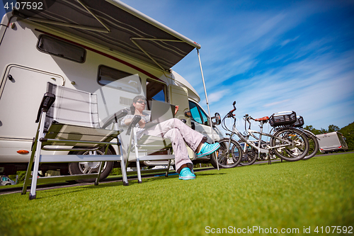 Image of Woman sitting on a chair near the camper and looking at a laptop