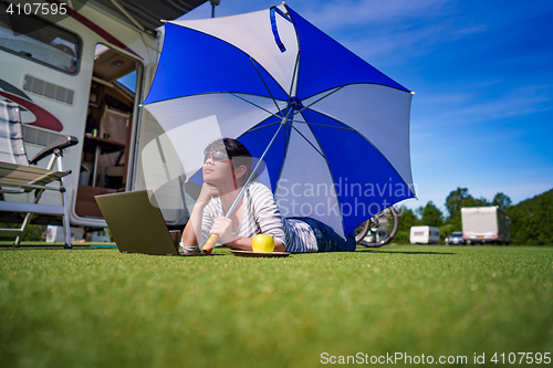 Image of Woman on the grass, looking at the laptop under umbrella near th