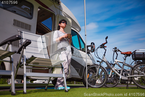 Image of Woman is standing with a mug of coffee near the camper.