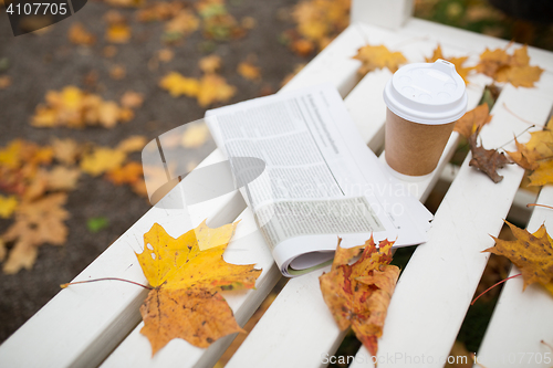 Image of newspaper and coffee cup on bench in autumn park