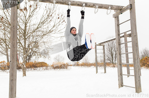 Image of young man exercising on horizontal bar in winter