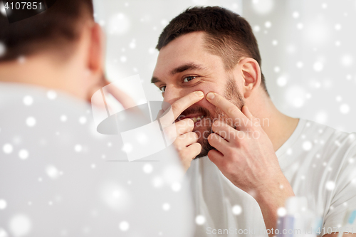 Image of smiling man squeezing pimple at bathroom mirror