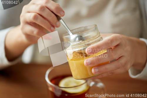 Image of close up of woman adding honey to tea with lemon