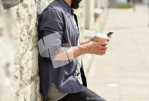 Image of man with smartphone drinking coffee on city street