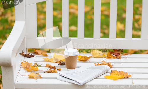 Image of newspaper and coffee cup on bench in autumn park