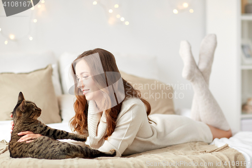 Image of happy young woman with cat lying in bed at home