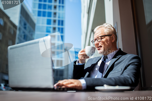 Image of senior businessman with laptop drinking coffee