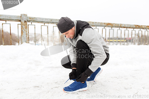 Image of man with earphones tying sports shoes in winter