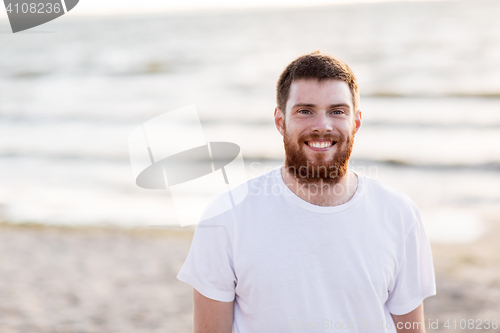 Image of happy smiling young man with red beard on beach