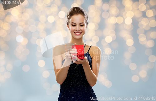 Image of smiling woman holding red gift box over lights