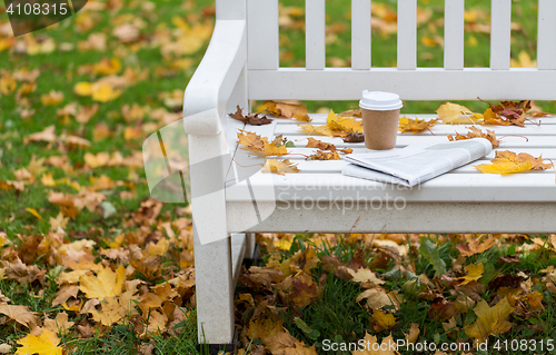 Image of newspaper and coffee cup on bench in autumn park