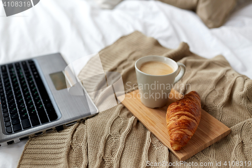 Image of laptop, coffee and croissant on bed at cozy home