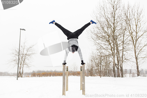 Image of young man exercising on parallel bars in winter