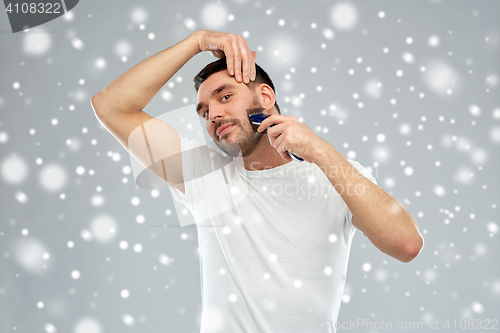 Image of smiling man shaving beard with trimmer over snow