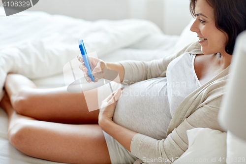 Image of close up of pregnant woman with smartphone in bed