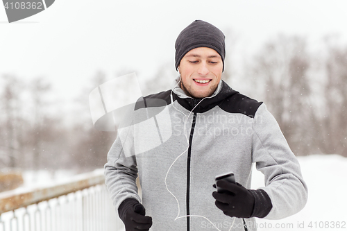 Image of happy man with earphones and smartphone in winter