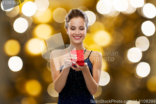 Image of smiling woman holding red gift box over lights