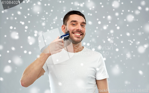 Image of smiling man shaving beard with trimmer over snow