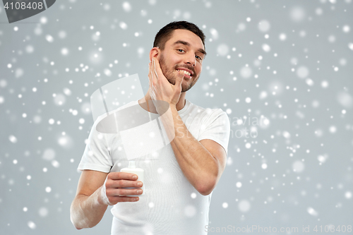 Image of happy young man applying cream or lotion to face