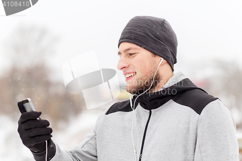 Image of happy man with earphones and smartphone in winter