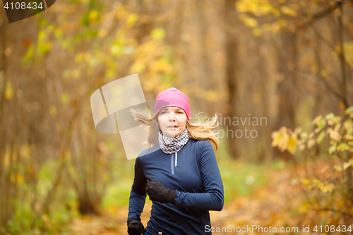 Image of Young blond woman athlete running in forest on autumn day