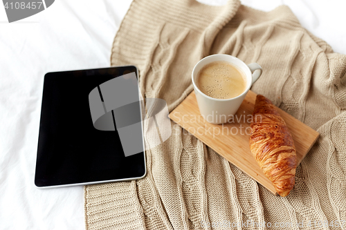 Image of tablet pc, coffee and croissant on bed at home