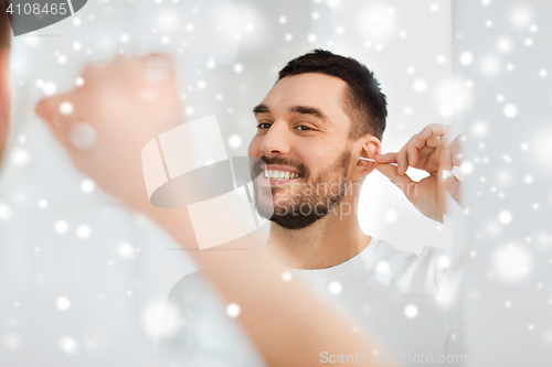 Image of man cleaning ear with cotton swab at bathroom