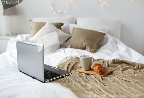 Image of laptop, coffee and croissant on bed at cozy home