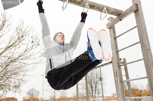 Image of young man exercising on horizontal bar in winter